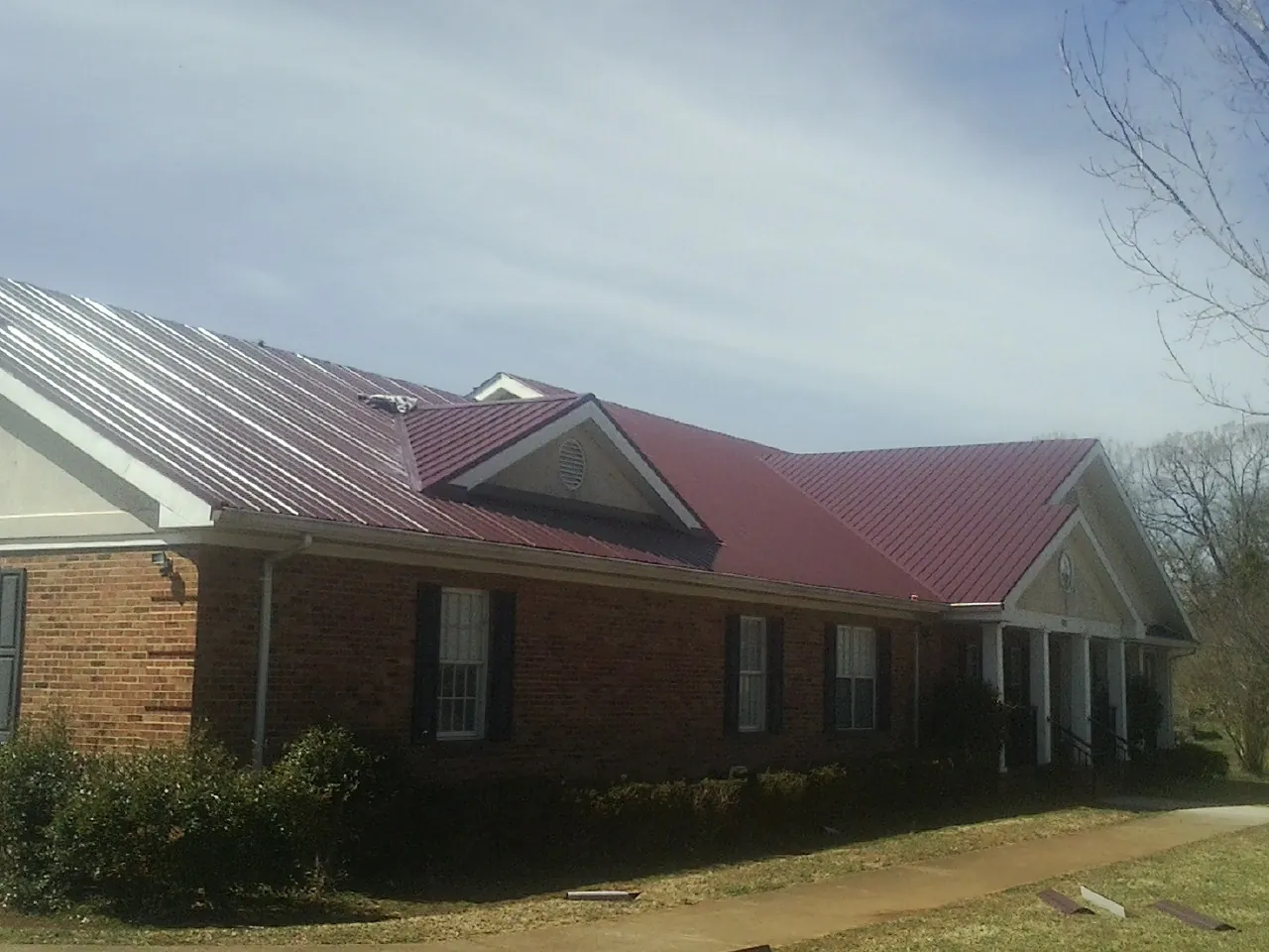 Red metal roof with gabled entries on a long brick building, from a Hail Damage Roof Repair job in Meyersdale