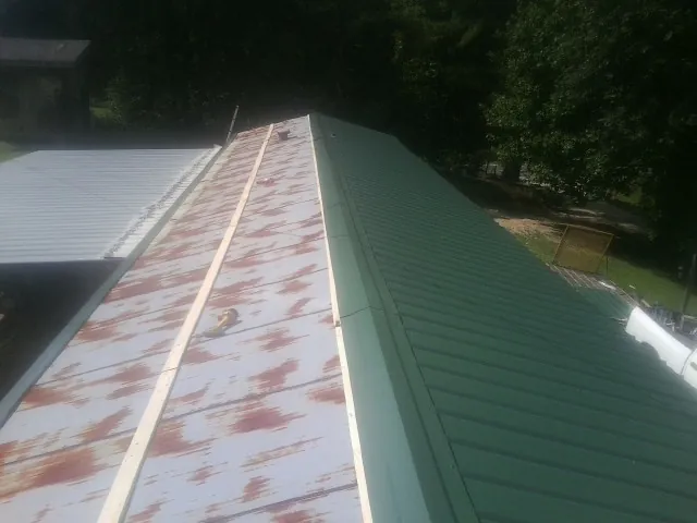 Old rusted panels beside newly installed green metal roofing — Wind Damage Roof Repair by Roofing Brothers in Meyersdale