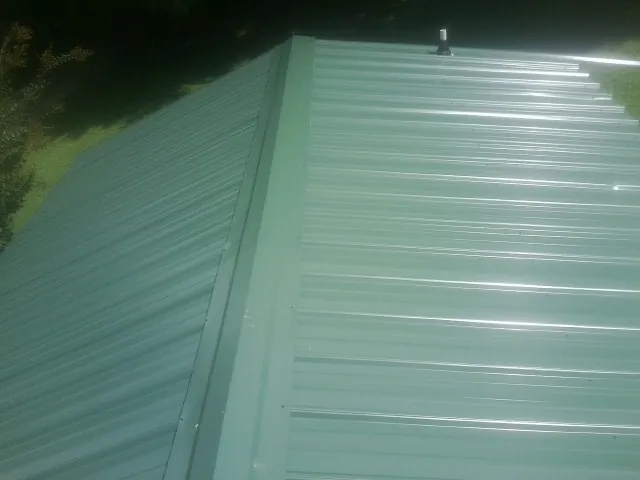 New green metal panels meeting at the ridge of a roof — Flat Roof Repair work by our crew in Meyersdale