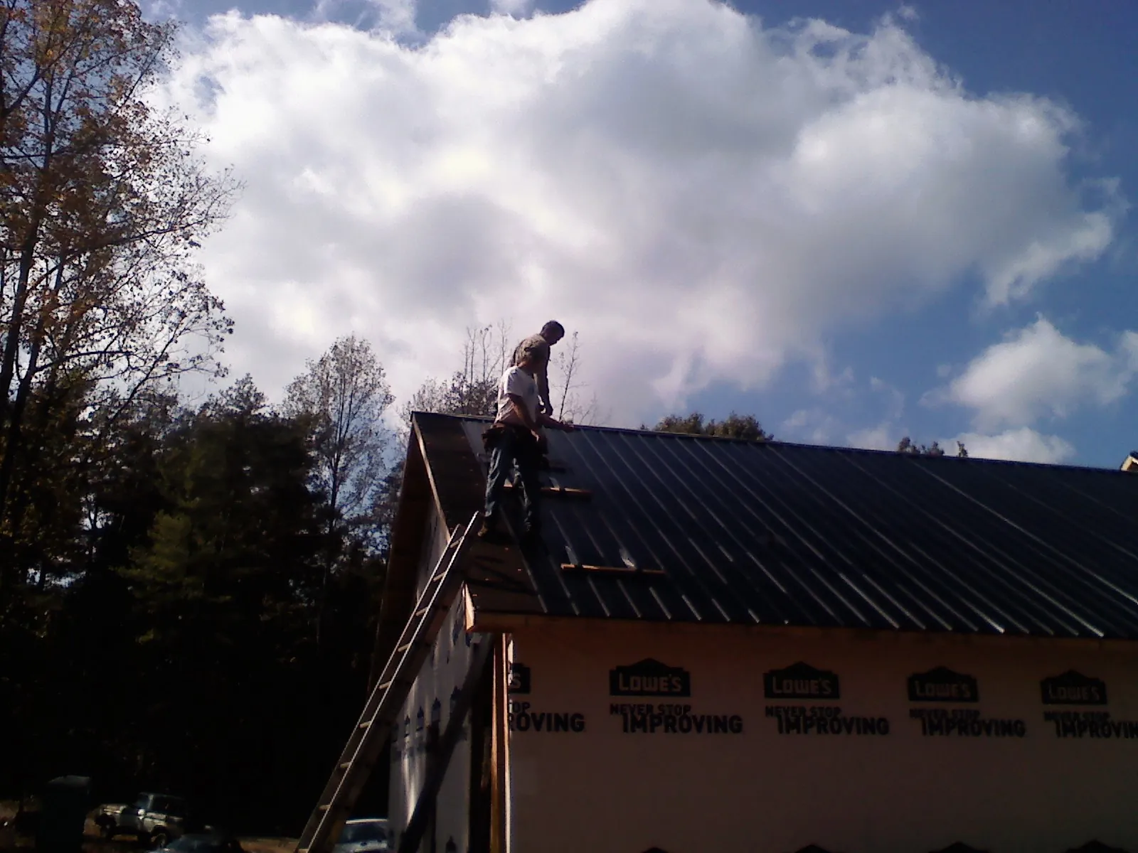 Roofer fastening dark metal panels high against a cloudy sky, from a Roof Inspection job in Meyersdale