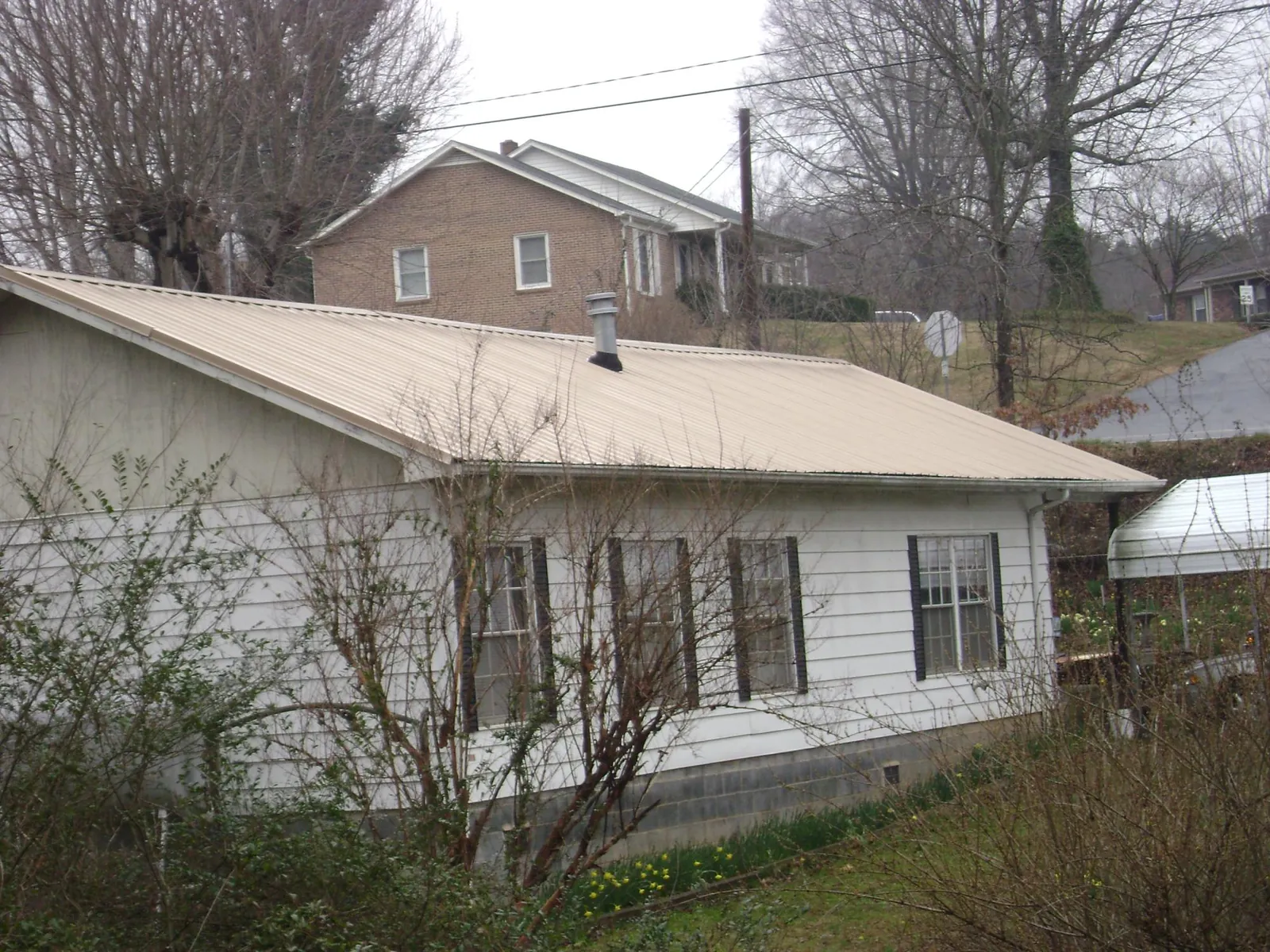 Tan metal roof on a white sided house set into a hillside — Commercial Roofing by Roofing Brothers in Meyersdale
